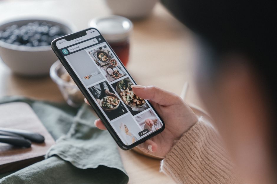 Pessoa navegando em um aplicativo de fotos de comida em um smartphone, com foco na interação digital e alimentação.