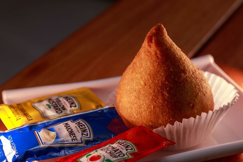 Imagem de um acarajé com pacotes de condimentos ao lado, simbolizando cultura e gastronomia afro-brasileira.