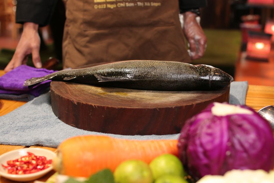 Imagem de um peixe fresco sobre uma tábua de corte, com vegetais ao redor, ideal para ilustrar gastronomia ou culinária saudável.