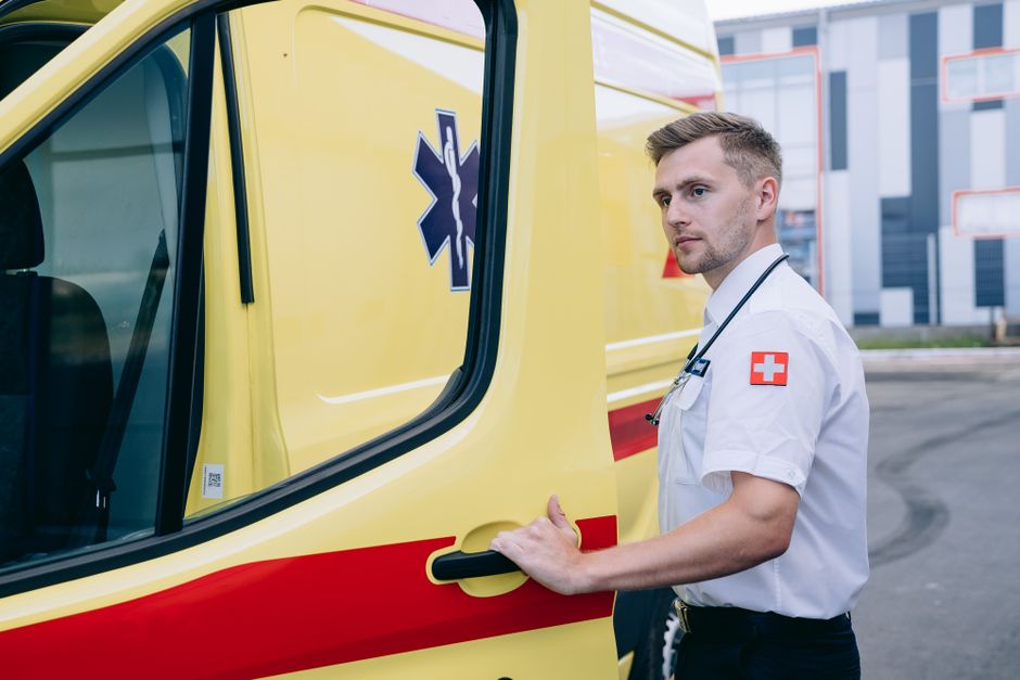 Profissional de saúde ao lado de ambulância, representando transporte de emergência e atendimento médico de urgência.