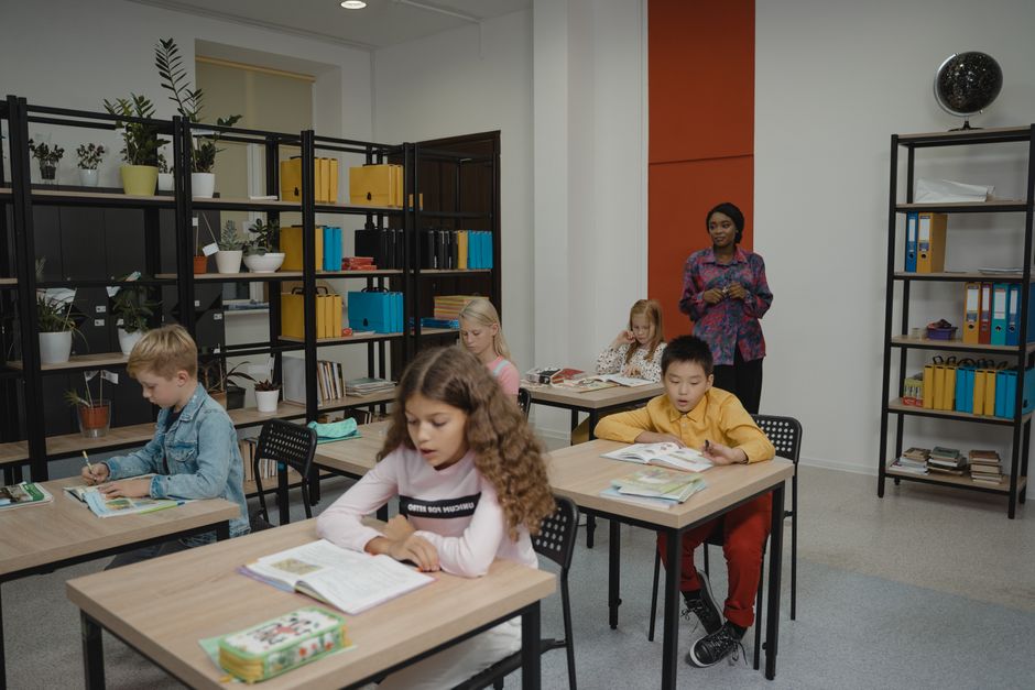 Grupo de crianças em sala de aula recebendo orientação de uma professora, promovendo o aprendizado e a educação infantil.