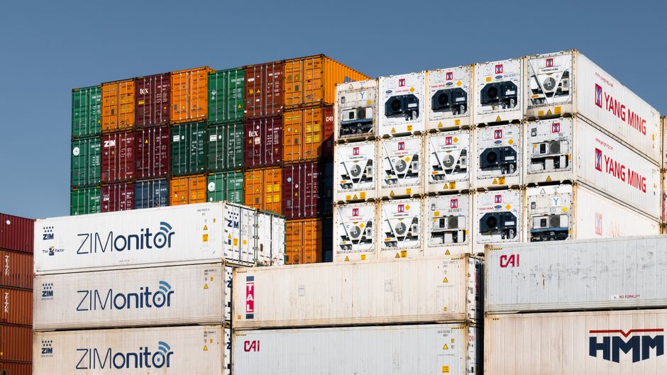 Imagem de contêineres de carga empilhados, representando logística e transporte internacional.
