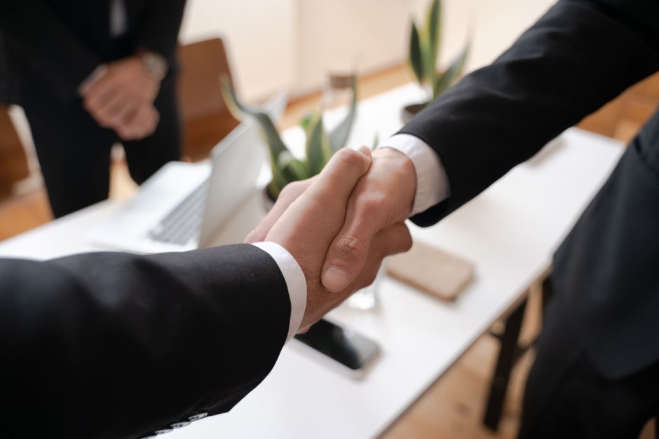 Duas pessoas apertando as mãos em um ambiente de negócios, simbolizando parceria ou acordo profissional.