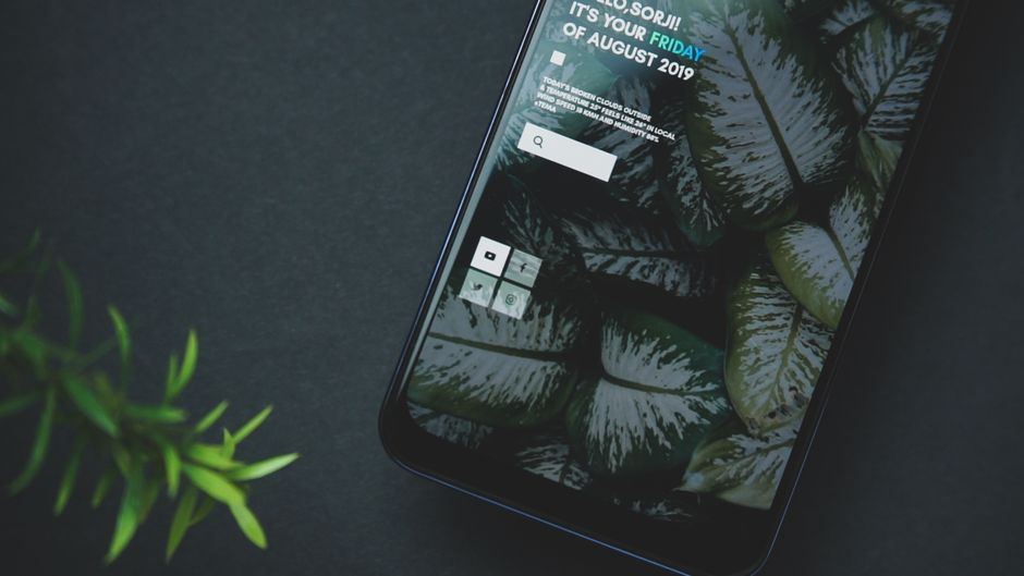 Imagem de um smartphone com uma tela que exibe um tema relacionado à organização pessoal ou aplicativos de produtividade, apoiado por uma planta ao lado.