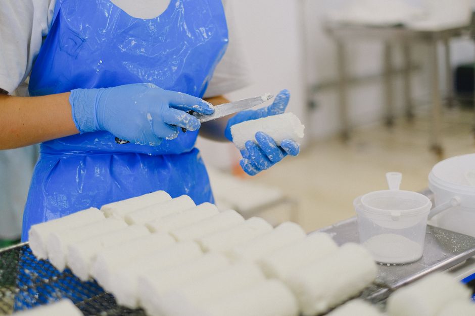 Pessoa preparando produtos alimentícios em uma cozinha industrial, com foco na produção artesanal de queijos ou doces. 