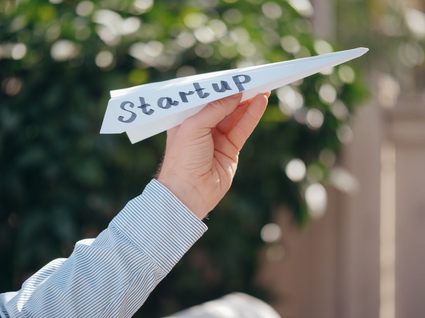 Pessoa segurando um avião de papel com a palavra 'start-up' escrita, simbolizando o conceito de empreendedorismo e inovação.