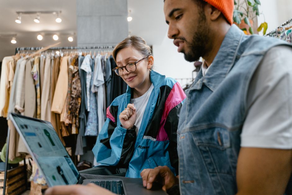 Dupla analisando tendências de moda em uma loja de roupas, focando em compras e estilo pessoal.