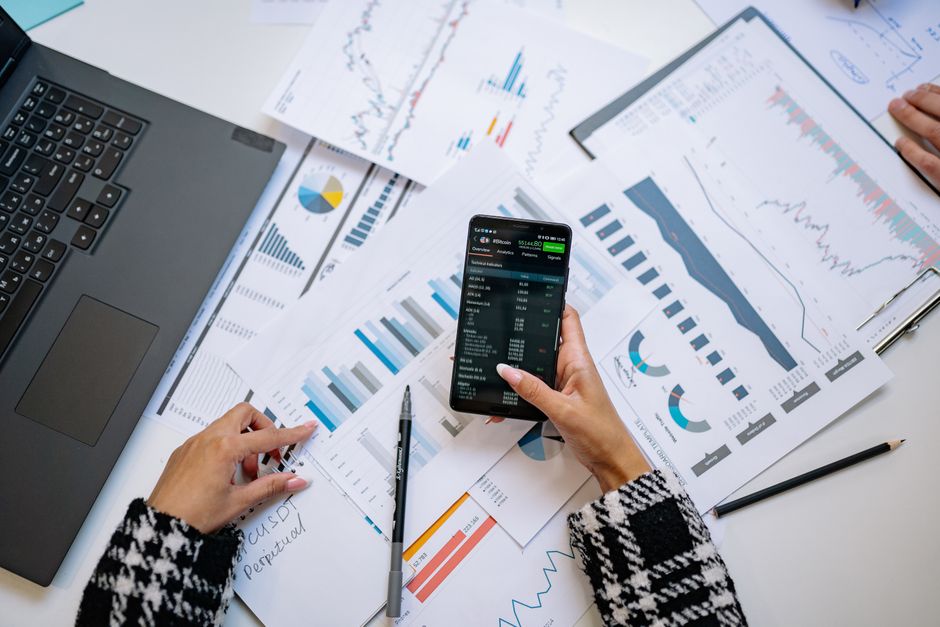 Profissional analisando dados financeiros e gráficos de desempenho em um ambiente de trabalho com várias planilhas e relatórios, ilustrando a importância da análise de informações para tomada de decisão.