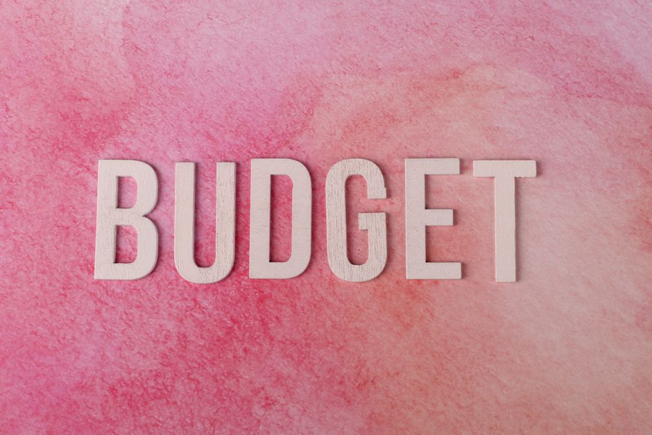 Imagem com letras em destaque formando a palavra 'BUDGET' sobre um fundo rosa, simbolizando planejamento financeiro e gestão de recursos.