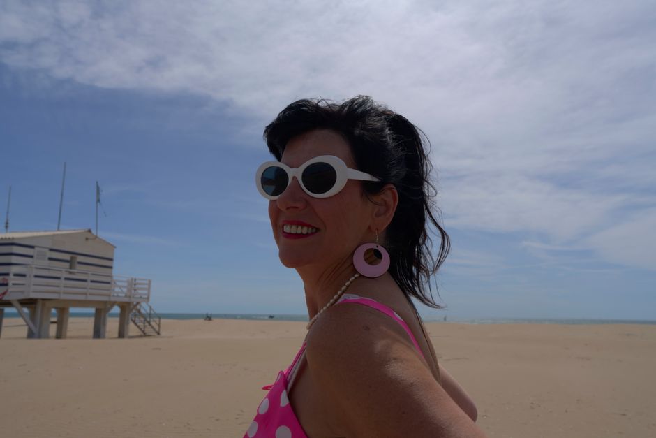 Mulher sorridente usando óculos de sol e roupa de praia em uma tarde ensolarada na areia da praia, transmitindo alegria e lazer ao ar livre.