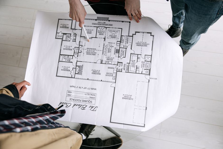 Pessoas analisando um projeto de planta baixa de uma residência, focando no planejamento arquitetônico.