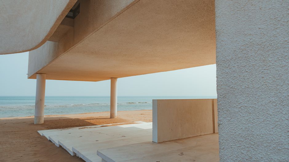 Imagem de um edifício moderno na praia, com arquitetura minimalista e vista para o mar, ideal para ilustrar temas de design, arquitetura ou turismo costeiro.