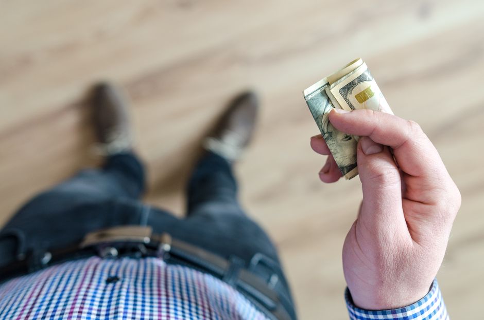 Pessoa segurando dinheiro na mão, com foco na ação de pagamento ou compra, visto de cima para baixo.
