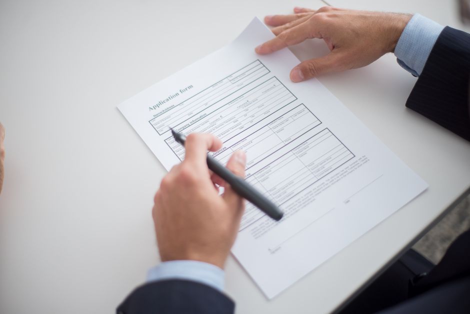 Imagem de uma pessoa assinando ou preenchendo um formulário de inscrição, simbolizando processos administrativos ou recrutamento em ambiente profissional.