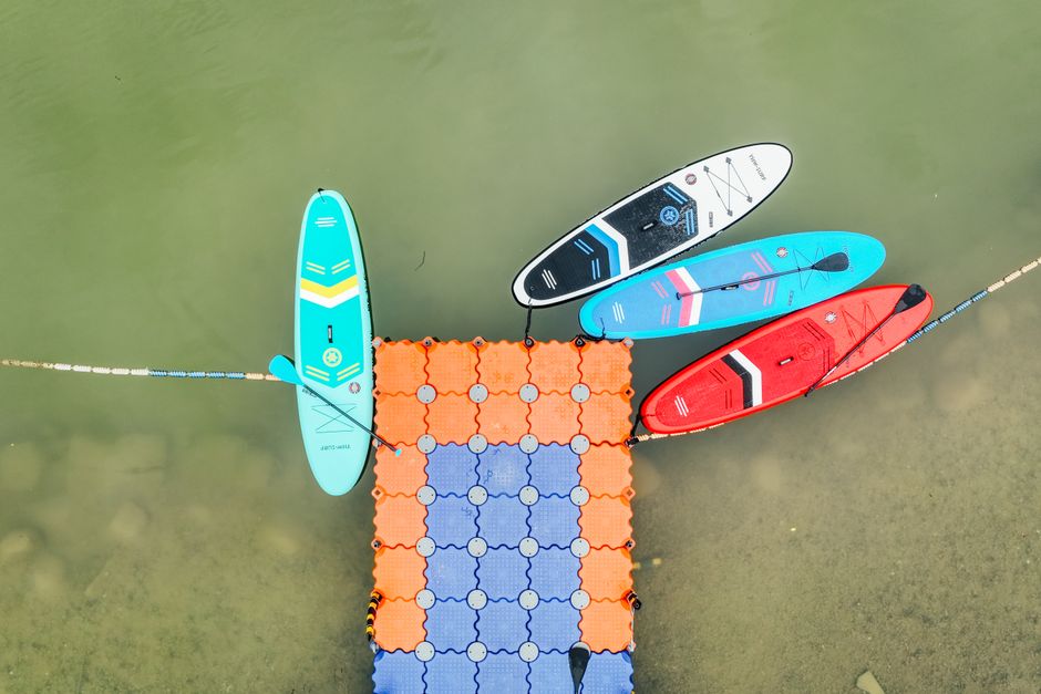 Imagem de pranchas de stand-up paddle e uma ponte de flutuação em uma atividade aquática ao ar livre, focada em lazer e esportes náuticos.