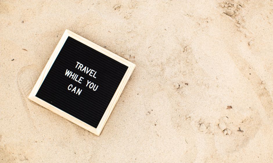 Quadro de aviso na areia com mensagem motivacional sobre viagens, ideal para artigos sobre viagens e aventuras ao ar livre.