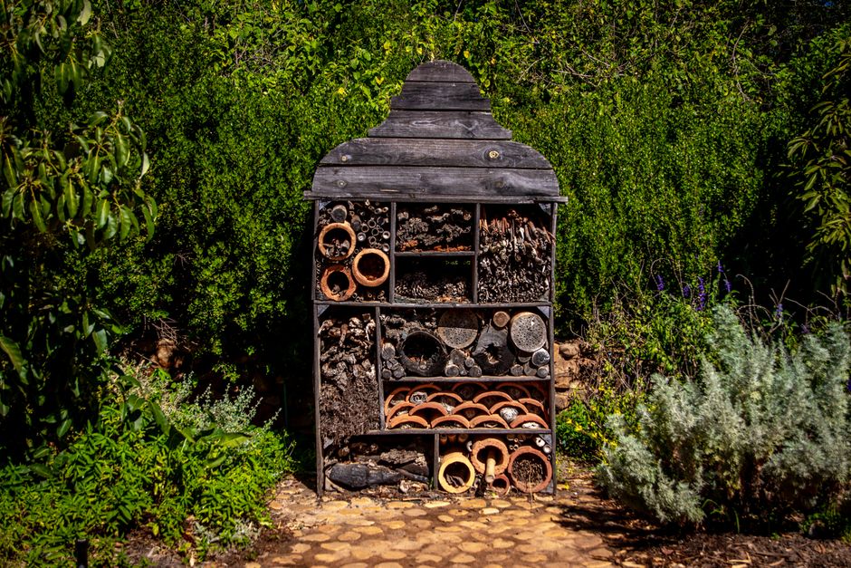 Estrutura decorativa de jardim feita com diversos elementos de terracota e pedaços de madeira, integrada ao ambiente natural ao redor.