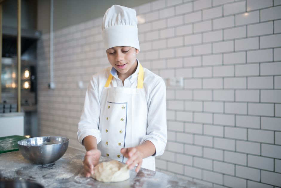 Jovem chef preparando massa em uma cozinha moderna, simbolizando educação culinária e criatividade na gastronomia.