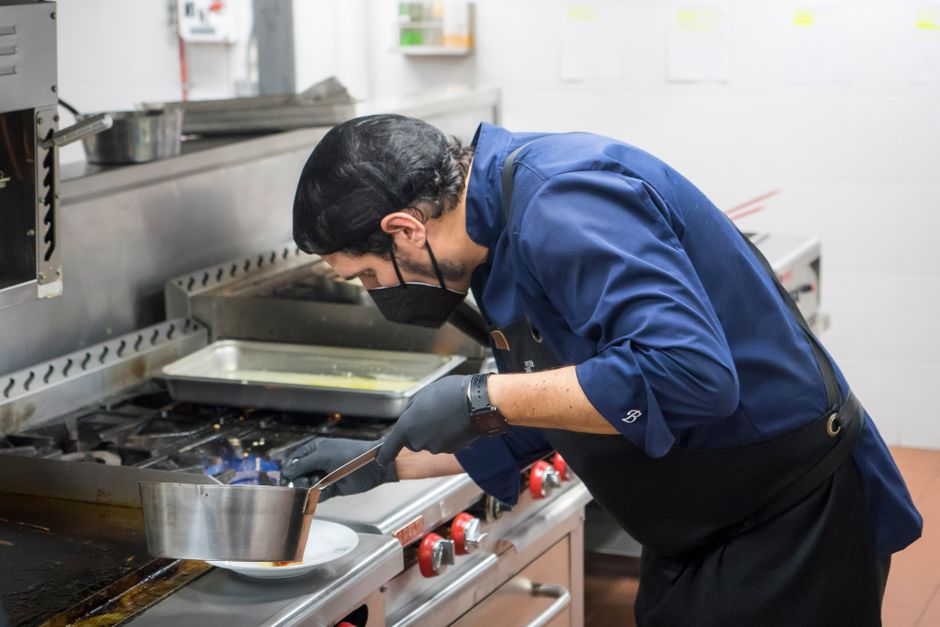 Chef profissional preparando um prato na cozinha de um restaurante, focado na arte culinária e técnica de cozinha profissional.