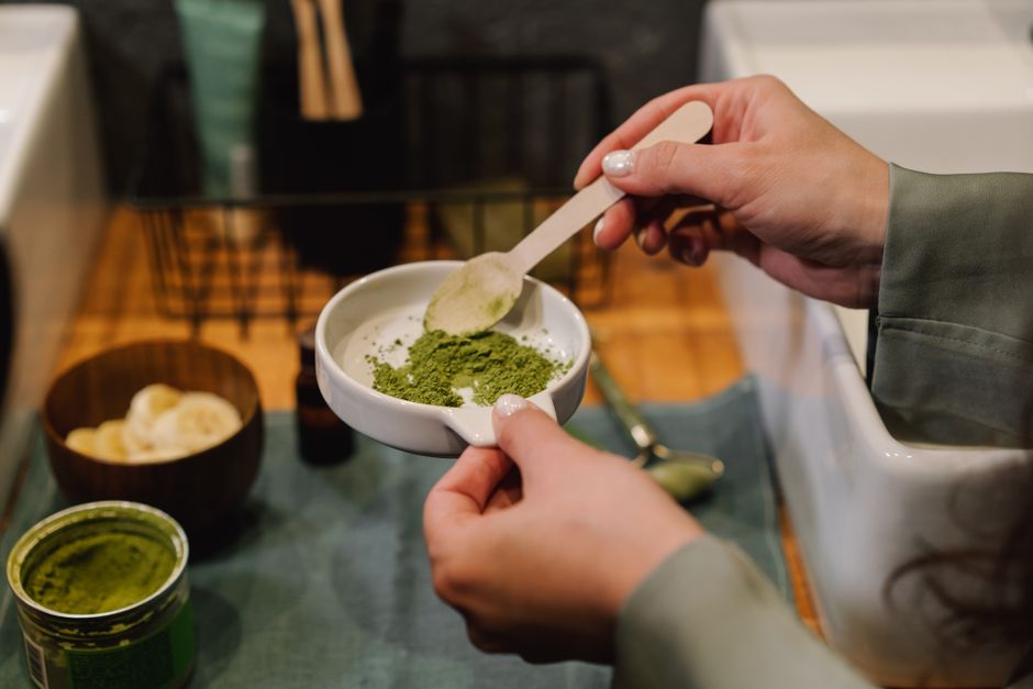 Pessoa preparando chá de matcha em um recipiente, destacando o processo de preparo de bebidas saudáveis.