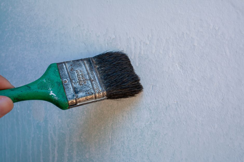 Pincel fazendo uma pintura ou aplicação de tinta em uma parede branca, simbolizando renovação ou decoração de ambientes.