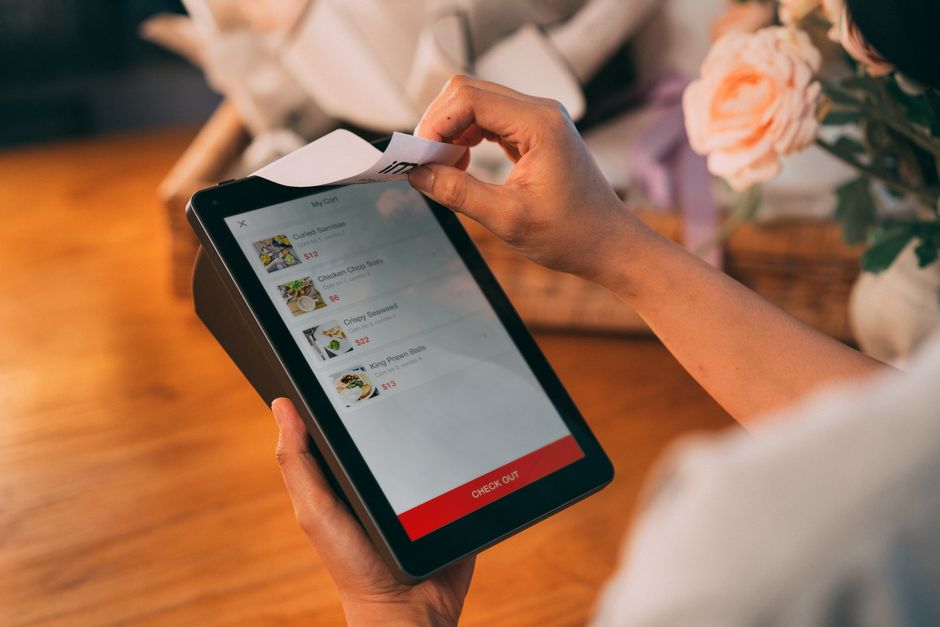Pessoa usando um tablet para realizar uma compra digital, ilustrando práticas modernas de pagamento e gestão de pedidos.