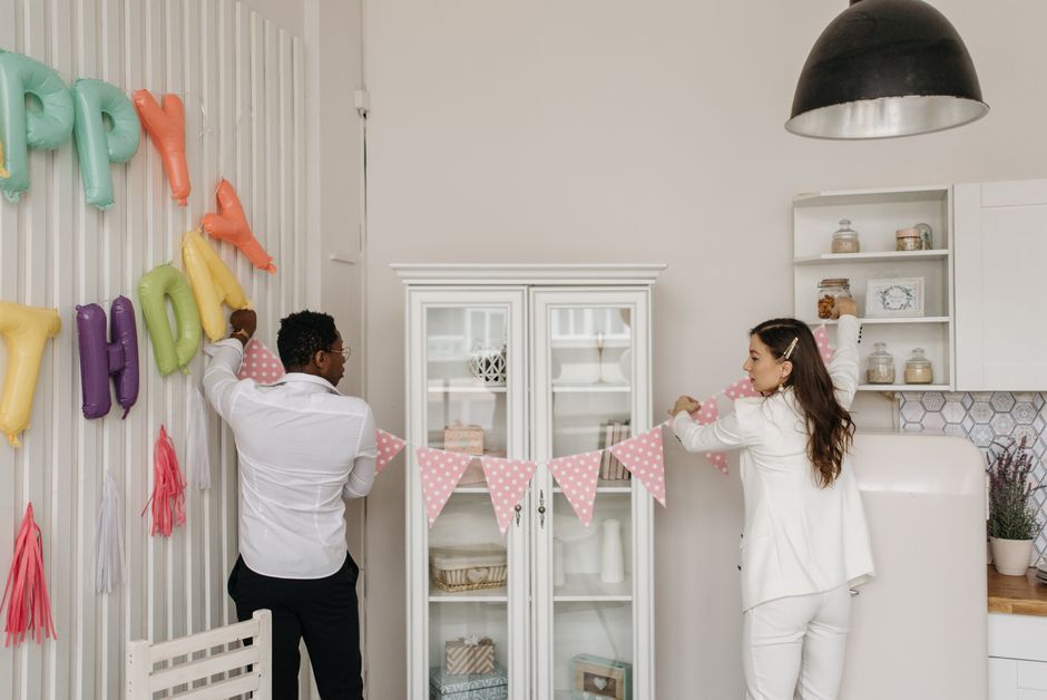 Casal decorando uma parede com balões e bandeirinhas em um ambiente festivo infantil, celebrando uma ocasião especial.