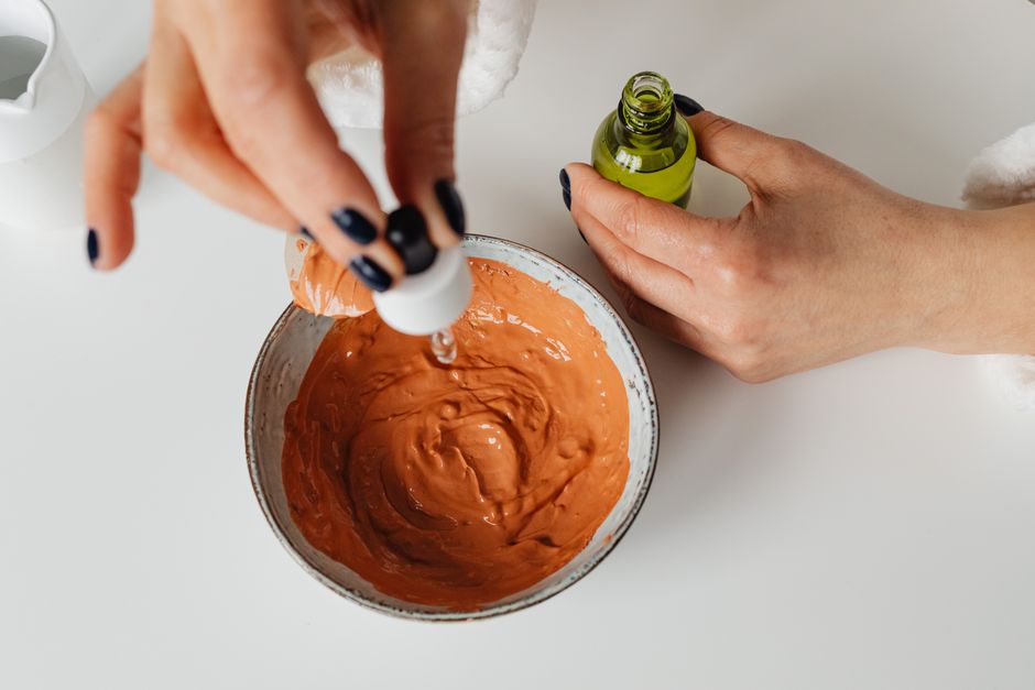 Imagem de uma pessoa misturando ingredientes em uma tigela, usando óleo essencial, em um contexto de cuidados pessoais ou aromaterapia.