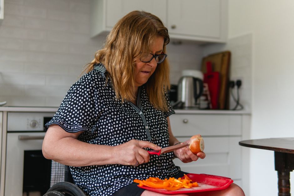 Mulher em cadeira de rodas preparando uma refeição com atenção na cozinha, refletindo inclusão e autonomia.