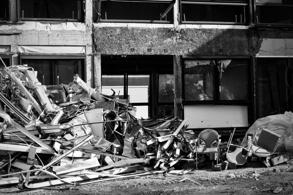 Imagem de edifício residencial parcialmente destruído com móveis e resíduos espalhados na fachada, indicando um cenário de desastre ou demolição.