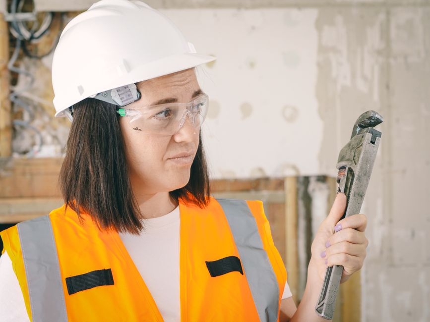 Mulher engenheira com equipamentos de segurança analisando uma ferramenta em obra, destacando a importância da fiscalização na construção civil.