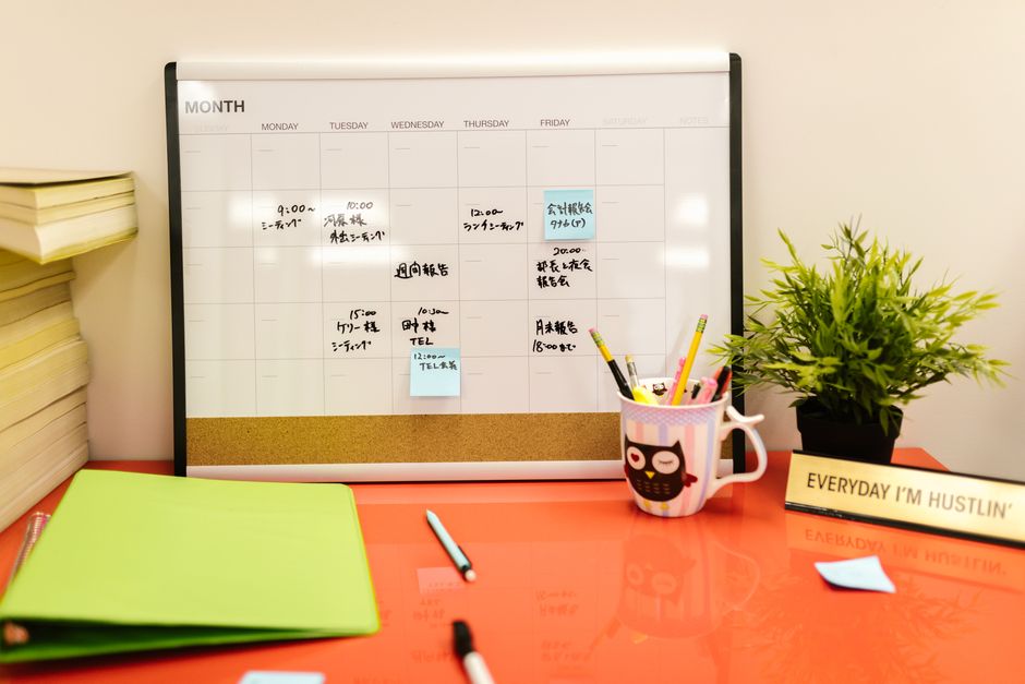 Canto de uma mesa de trabalho com agenda, canetas, uma planta e uma xícara decorada, criando um ambiente organizado e criativo para produtividade diária.