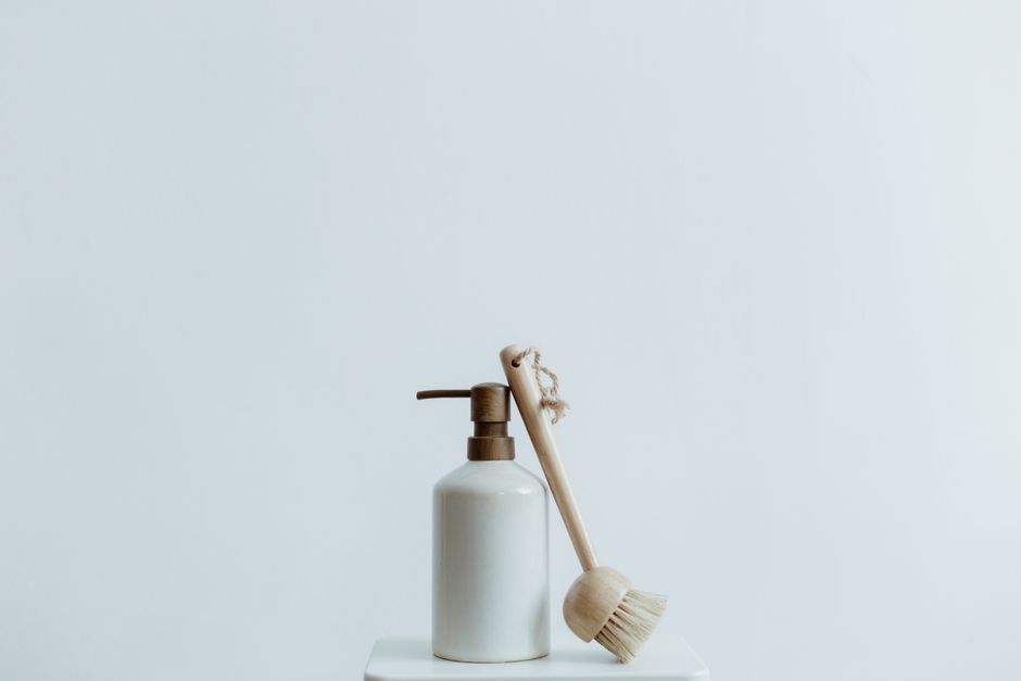Imagem minimalista de um dispenser de sabonete líquido ao lado de uma escova de limpeza, simbolizando higiene e cuidados domésticos.
