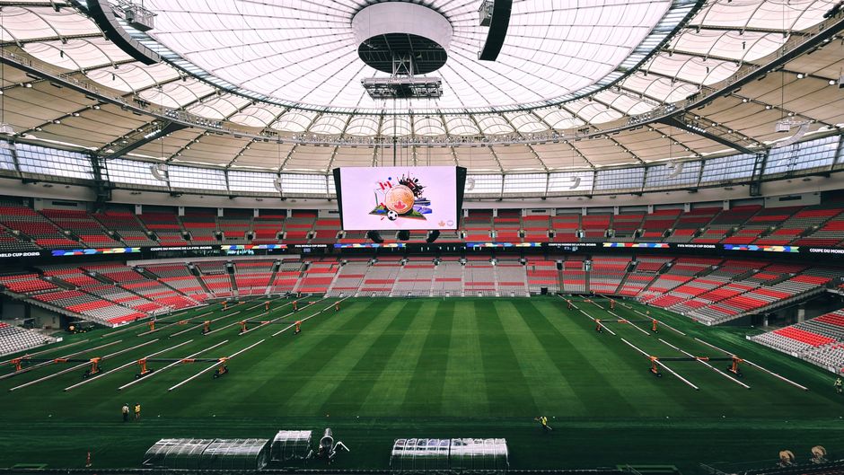 Imagem de um estádio de futebol com gramado bem cuidado e telão central, preparado para uma grande competição esportiva.