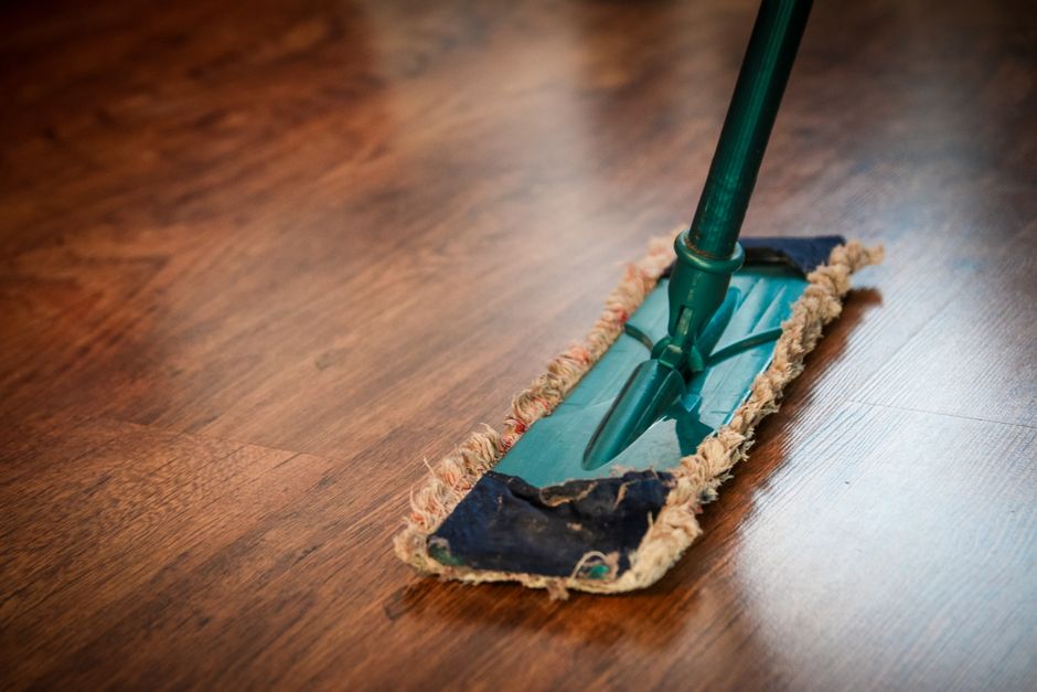 imagem de um rodinho de limpeza sendo usado em um piso de madeira para remoção de sujeira e poeira.