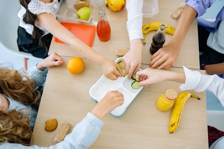Imagem de crianças em uma aula de culinária saudável, preparando lanches com frutas e legumes.