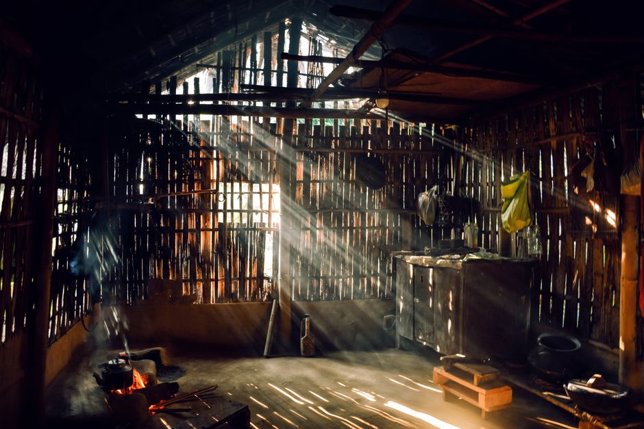  Interior de uma casa rústica com luz filtrando pelas frestas das paredes de madeira, criando um ambiente simples e aconchegante.