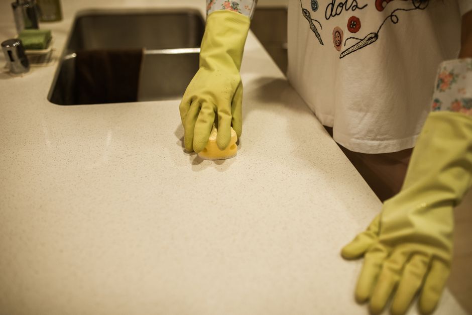 Pessoa limpando a bancada da cozinha com luvas de borracha, destacando a limpeza e organização do espaço culinário.