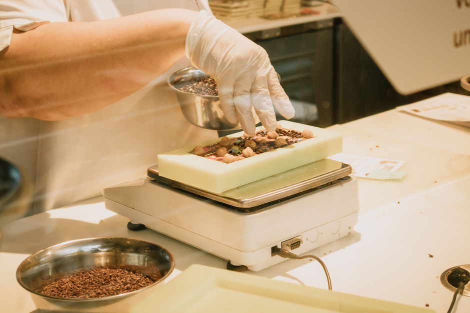 Pessoa decorando uma barra de chocolate com pedras de chocolate em uma mesa de cozinha.
