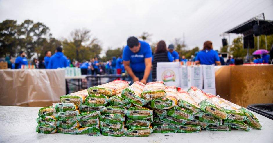  Pessoas participando de um evento ao ar livre, distribuindo alimentos e interagindo em um ambiente de comunidade e solidariedade.