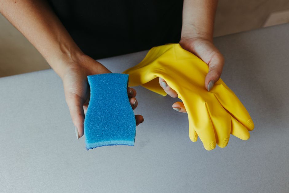 Imagem de duas mãos, uma com uma esponja azul e outra com uma luva amarela, simbolizando limpeza e higiene.