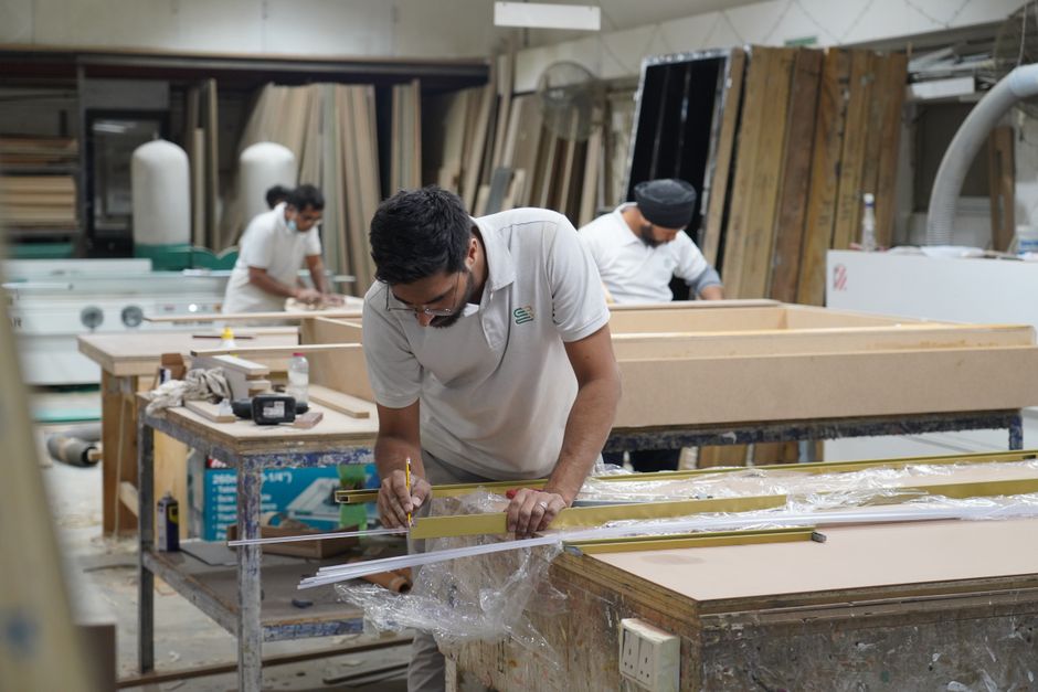Grupo de trabalhadores montando móveis em uma oficina de marcenaria, focada na produção artesanal e industrial de móveis.