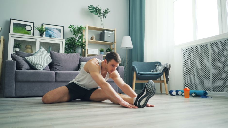 Homem realizando alongamento e exercícios de Yoga em ambiente doméstico, promovendo bem-estar e saúde na rotina diária.
