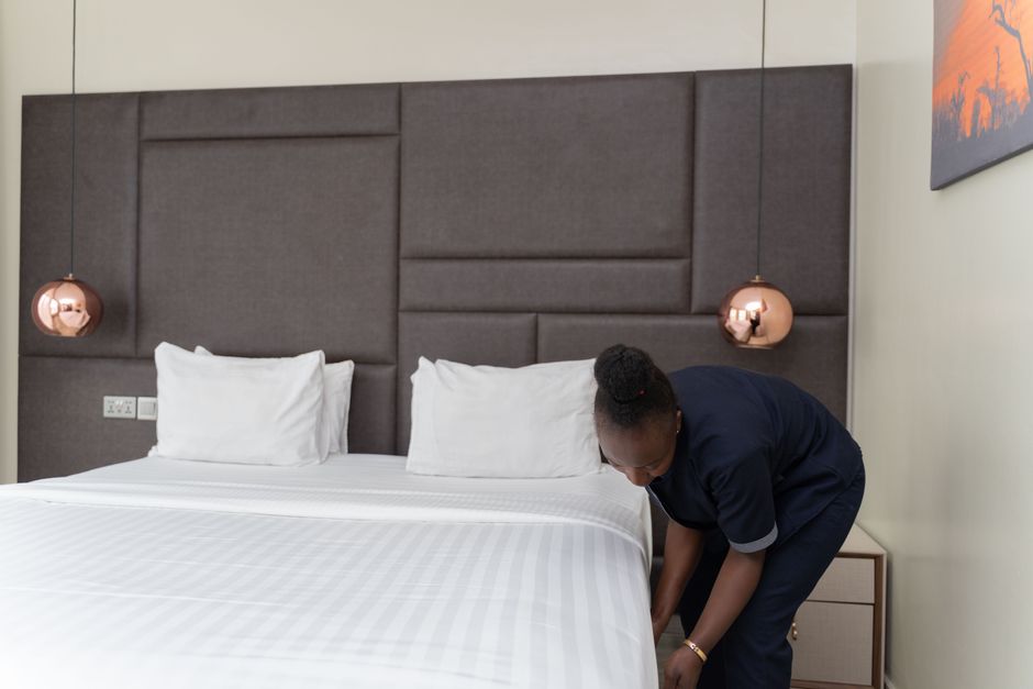 Uma profissional organizando a cama em um quarto de hotel, mostrando atenção aos detalhes para proporcionar conforto ao hóspede.