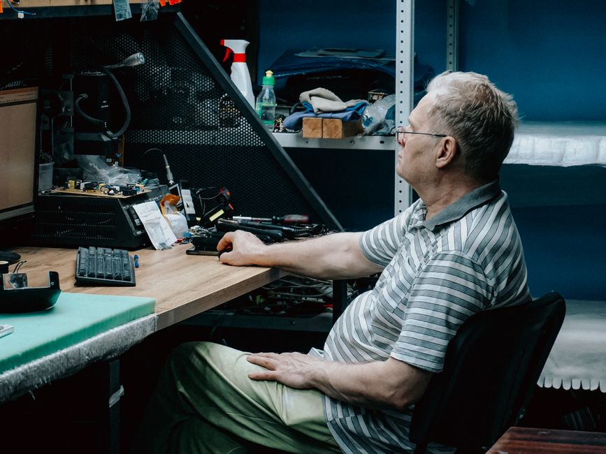 Homem trabalhando em uma bancada de montagem de eletrônicos em um ambiente de oficina ou laboratório técnico.