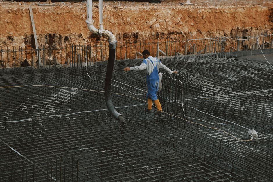 Profissional de construção civil trabalhando na preparação da estrutura de um edifício, com foco na execução de fundações usando armação de aço.