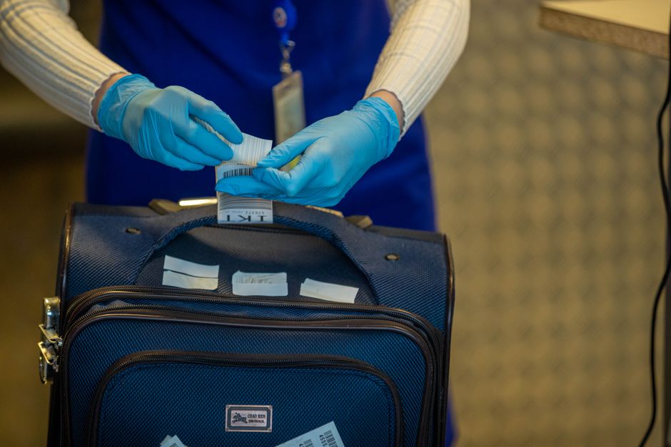 Pessoa colocando etiqueta em bagagem de mão, preparada para viagem ou transporte de documentos, focando na organização de itens pessoais ou profissionais.