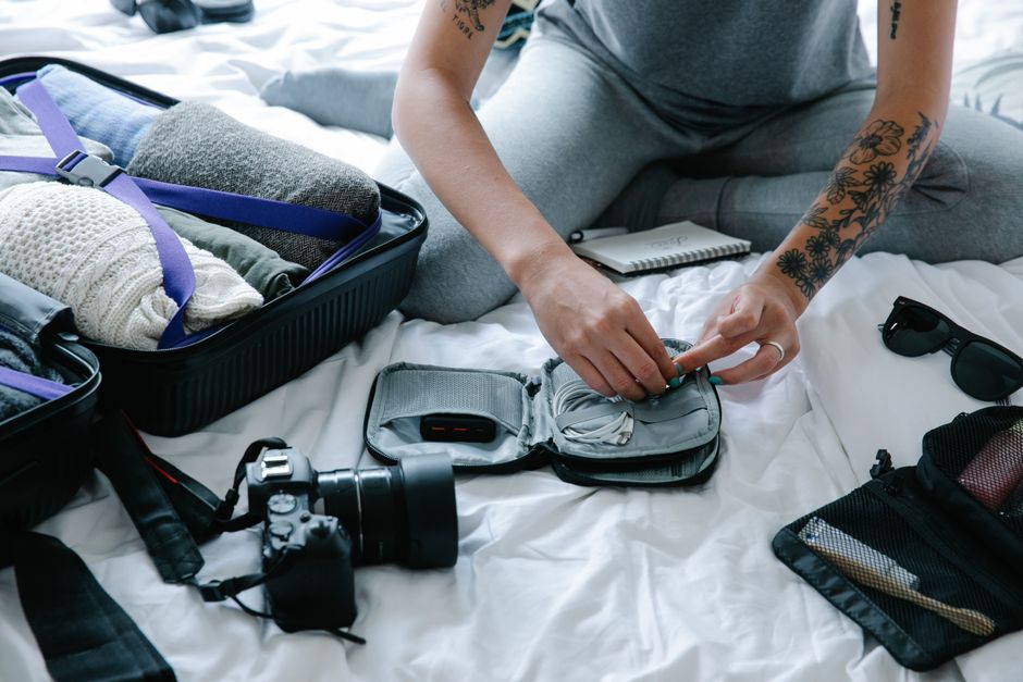 Pessoa organizando itens pessoais para viagem em um ambiente confortável, com câmera e acessórios de fotografia ao redor.