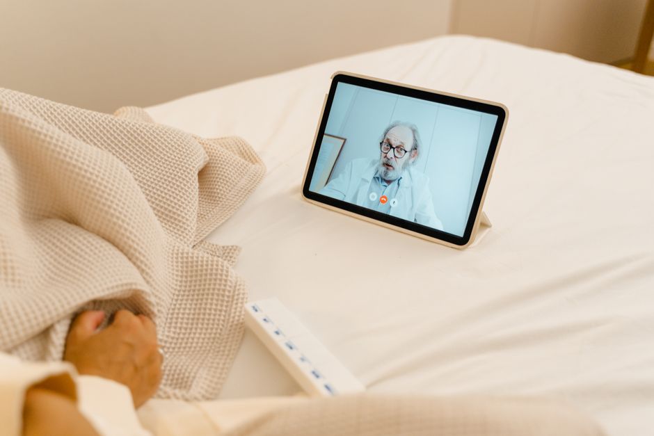 Paciente realizando consulta médica à distância usando tablet enquanto está deitado na cama.