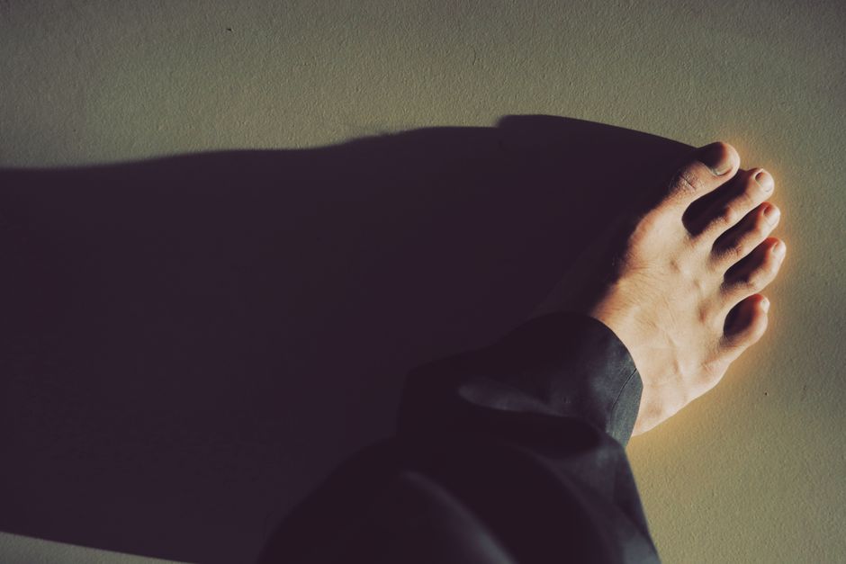 Mão de pessoa tocando uma parede com uma luz difusa, transmitindo um sentimento de introspecção ou reflexão.